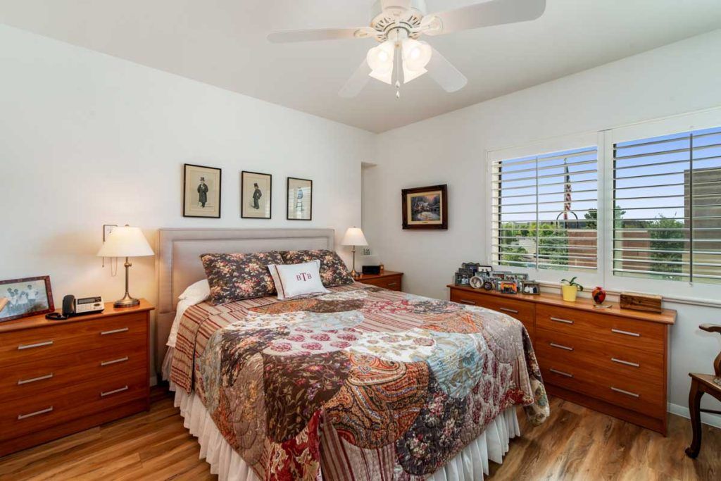 A cozy bedroom with a quilt-covered bed, wooden nightstands, and a ceiling fan.