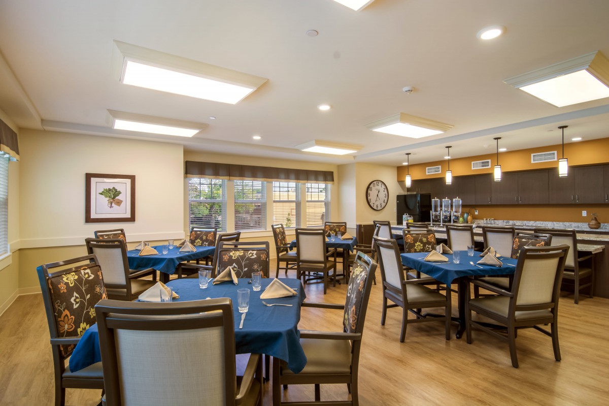 A modern dining area with neatly arranged tables and blue tablecloths, featuring overhead lighting.