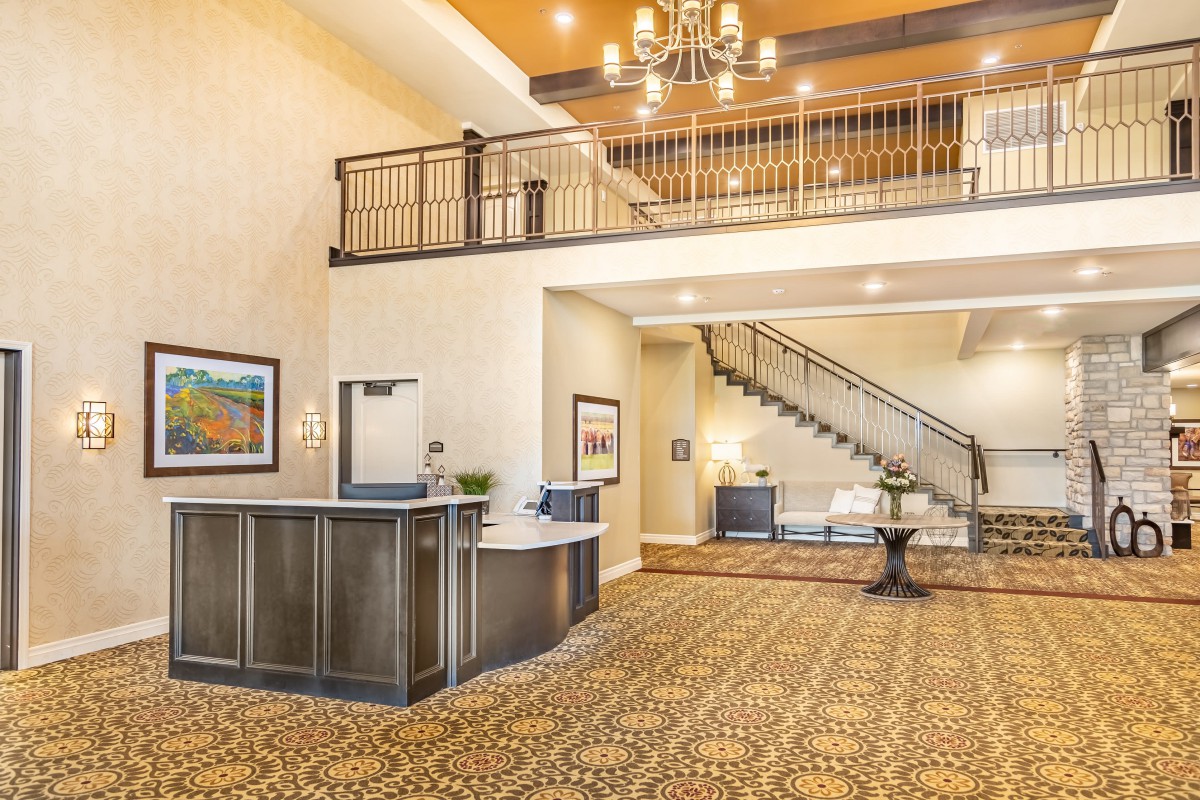 A spacious hotel lobby with a reception desk, staircase, and elegant chandelier.