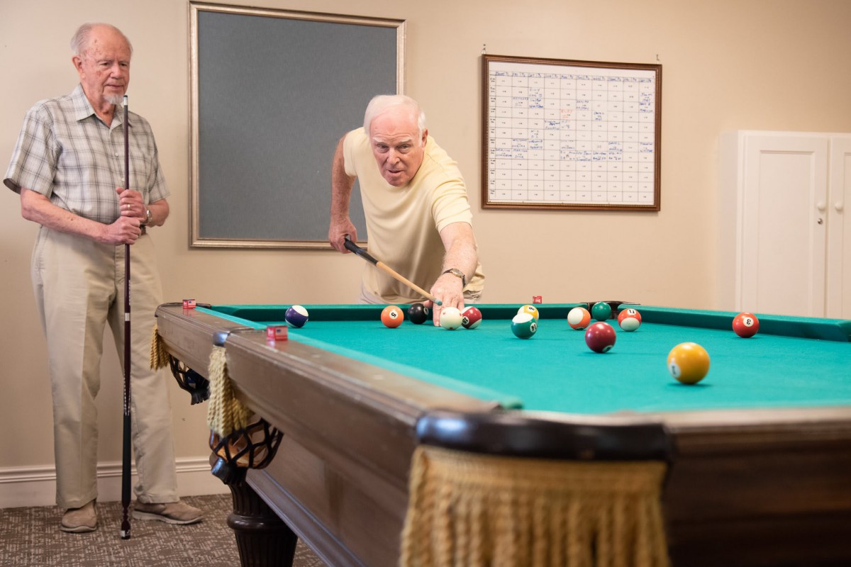An older man playing billiards on a pool table indoors.