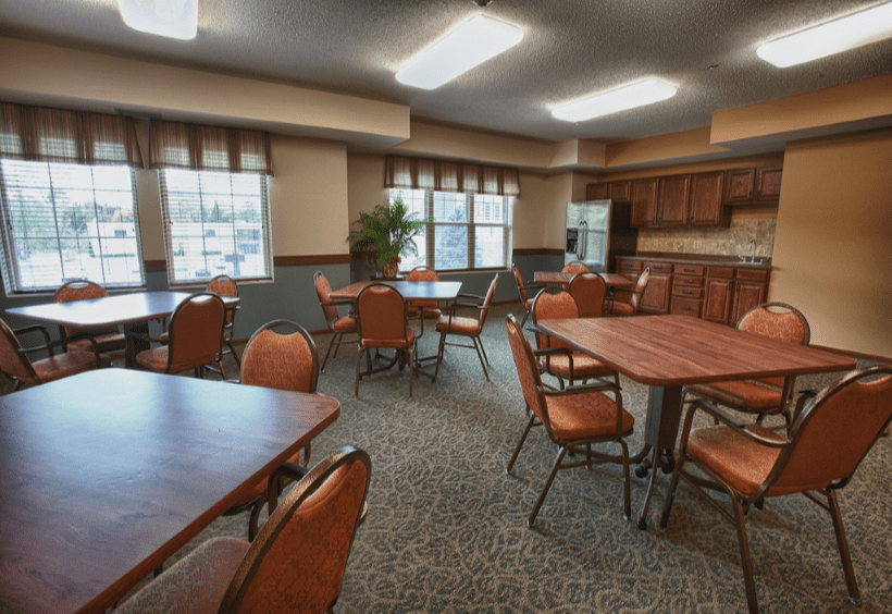 A cozy dining area with multiple tables and chairs, accompanied by a kitchenette and large windows.