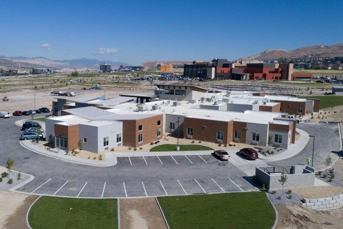 Aerial view of a modern building with a spacious parking lot, set against an urban backdrop.