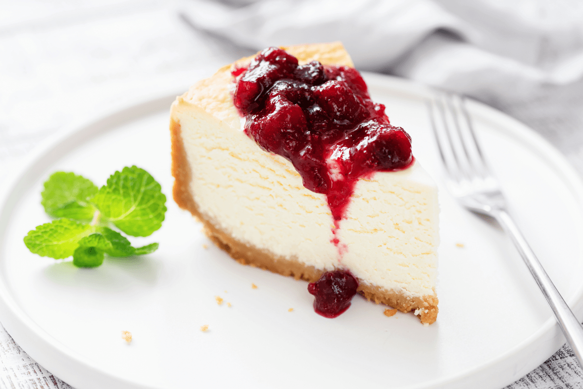 A slice of cheesecake topped with berry sauce and garnished with mint on a white plate.