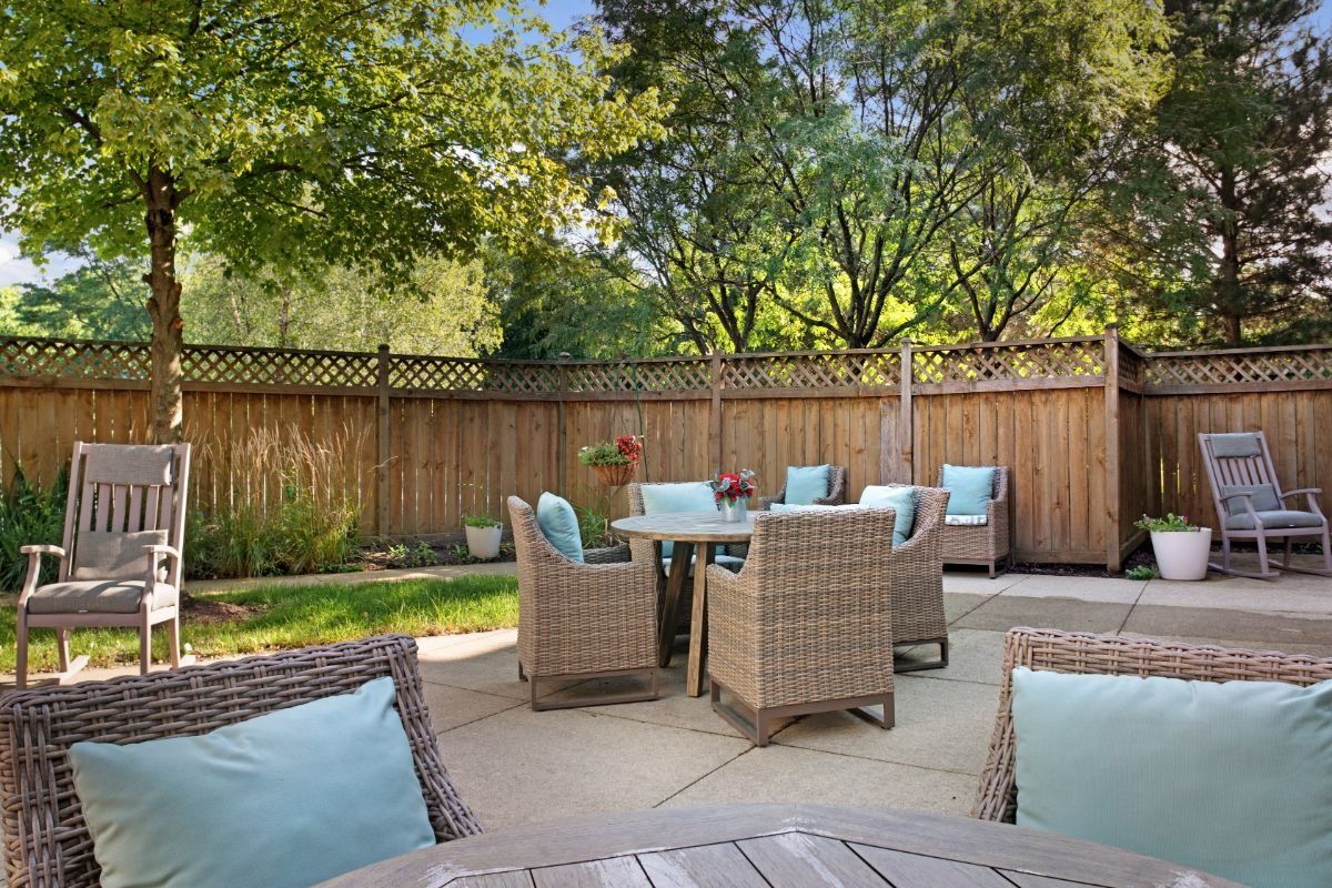 A cozy outdoor patio with wicker furniture and blue cushions surrounded by a wooden fence and lush trees.