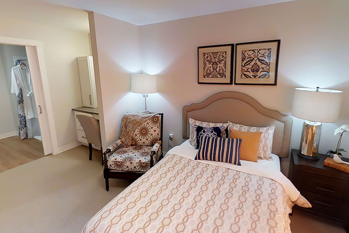 A cozy bedroom with a neatly made bed, decorative pillows, and a patterned armchair beside a floor lamp.
