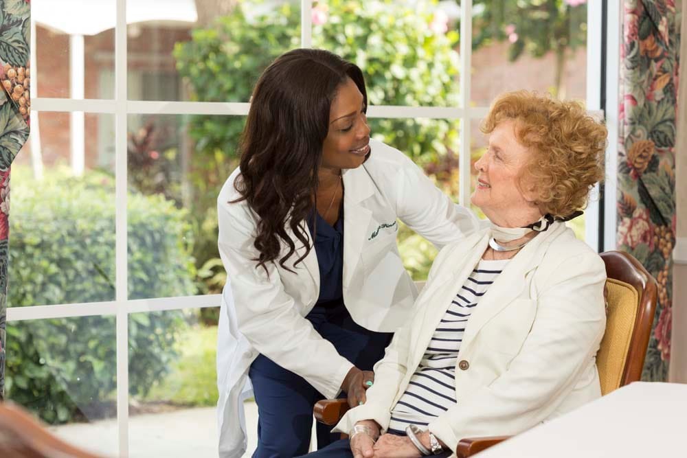 A doctor converses with an elderly patient in a bright, indoor setting.