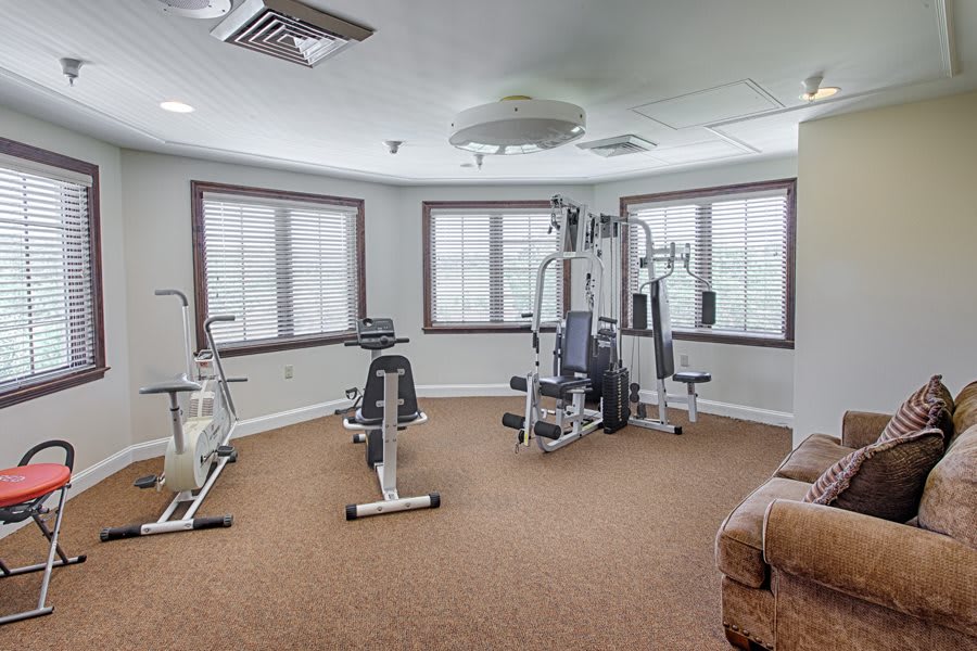 A well-lit home gym with various exercise equipment and large windows.