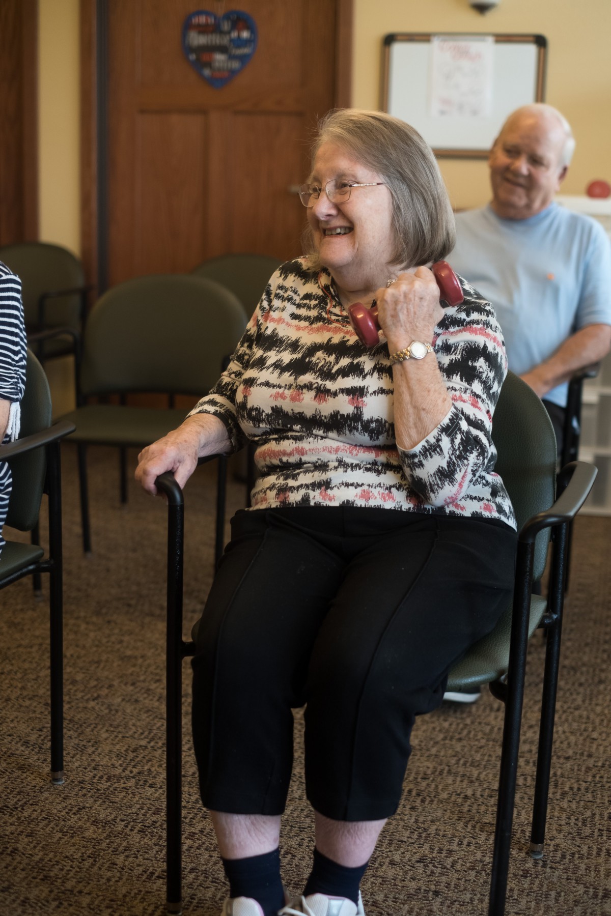 A group of seniors engaging in an indoor activity, sitting in chairs and smiling.