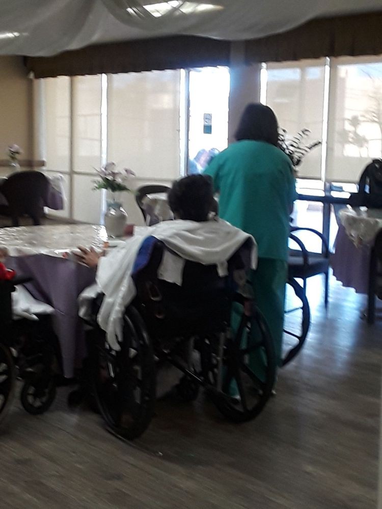 A caregiver tending to a person in a wheelchair in a nursing home setting.