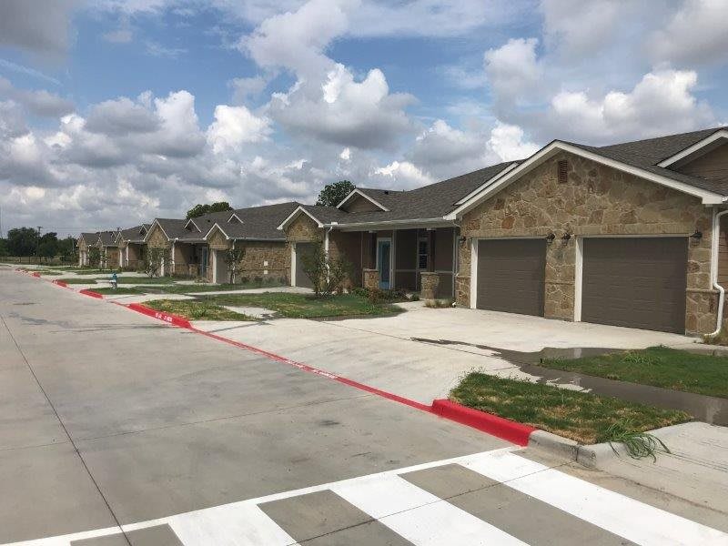 A row of suburban houses with driveways and garages under a cloudy sky.