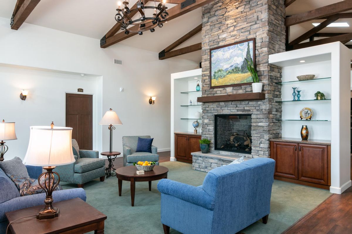A cozy, well-decorated living room featuring a stone fireplace, comfortable seating, and elegant wood beams.