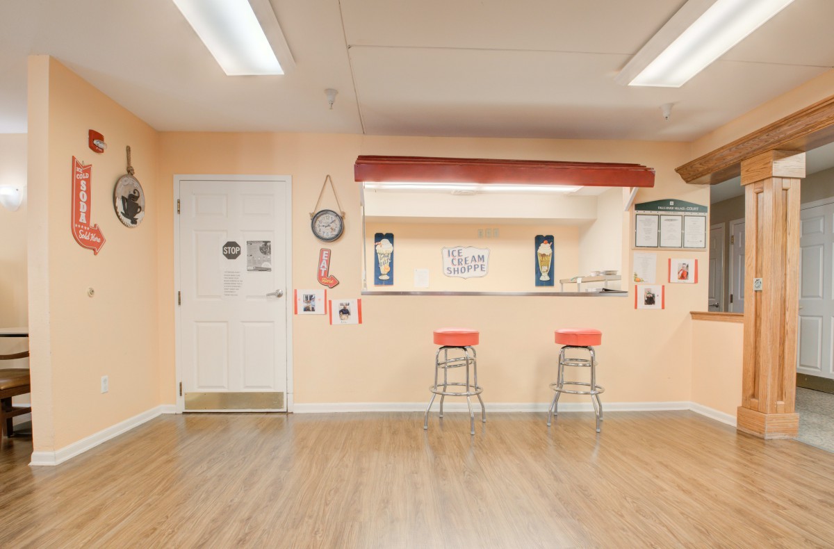 A brightly lit room with a counter and bar stools, featuring wooden flooring and wall decor.