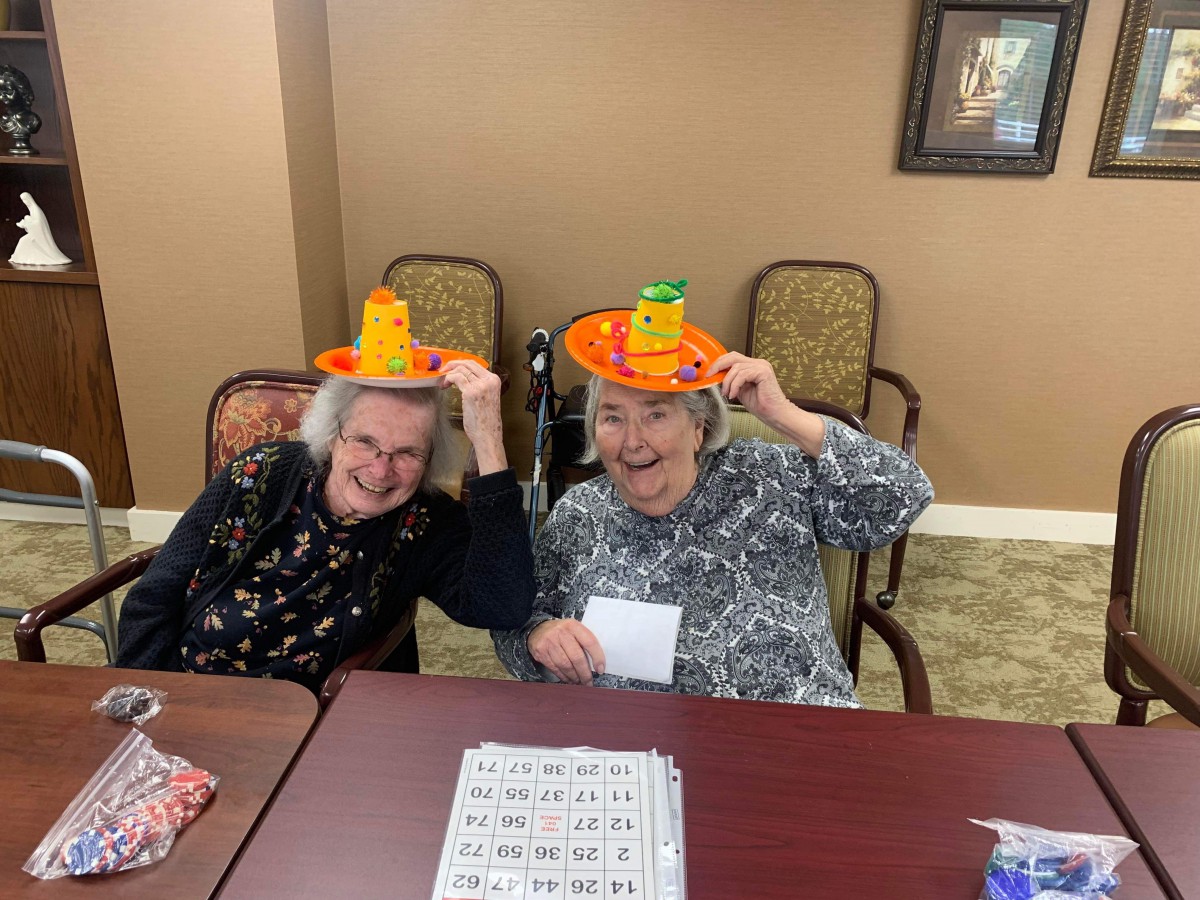 Two elderly women having fun with colorful hats while playing bingo.