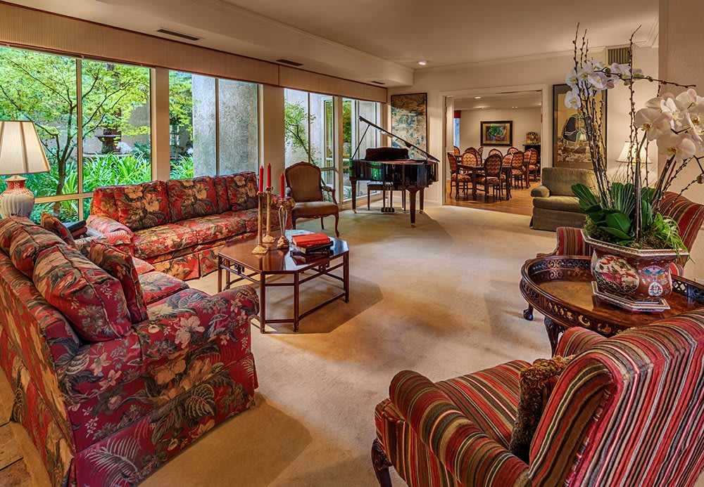 A cozy living room with floral and striped furniture, a grand piano, and an adjoining dining area.