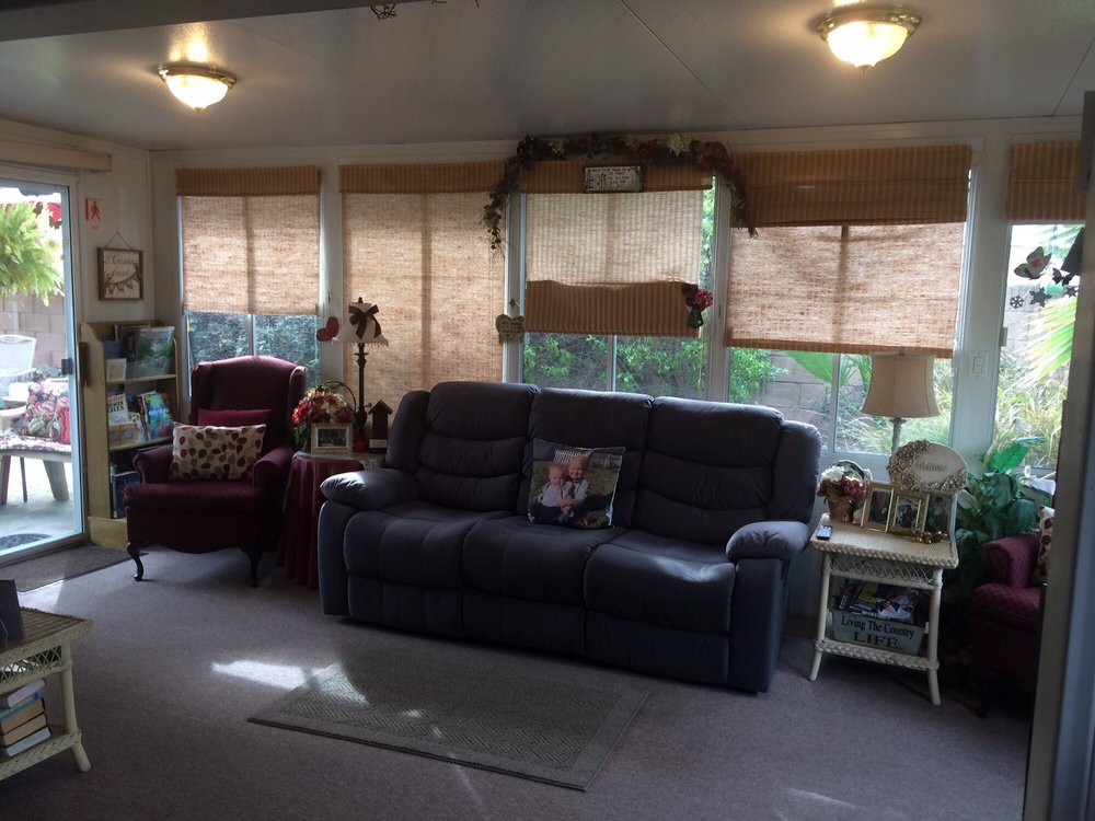 A cozy living room featuring a sofa, armchair, and large windows with blinds.
