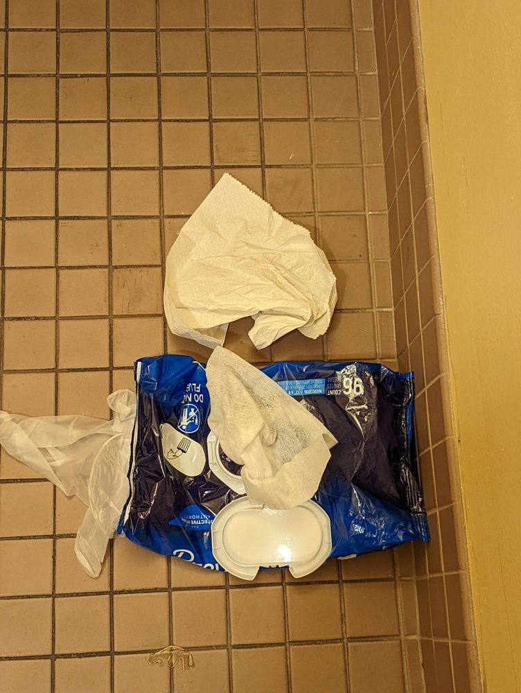 A bathroom scene with discarded paper towels on the tiled floor.