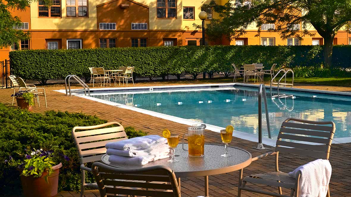 A relaxing outdoor pool area with chairs, a table, and refreshments on a sunny day.