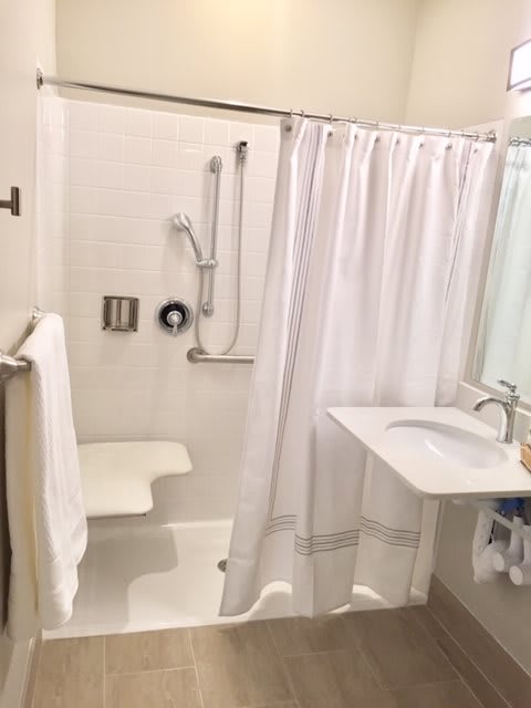 An accessible bathroom with a shower chair, grab bars, and a sink.