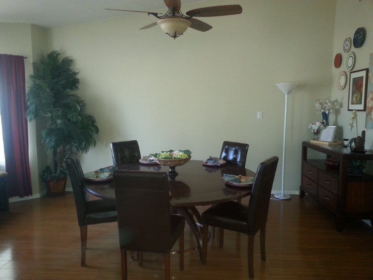 A dining room setup with a circular table and chairs, featuring a ceiling fan and indoor plant.