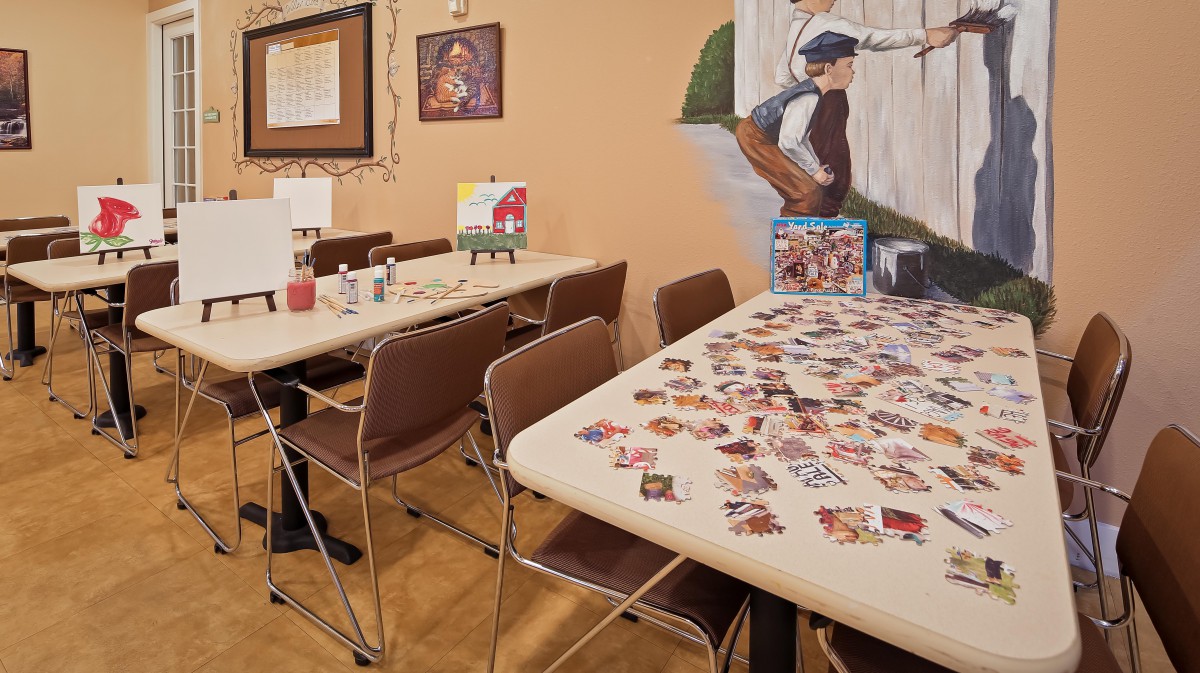 A cozy indoor space with tables set up for board games, featuring artwork on the walls and puzzle pieces spread across a table.