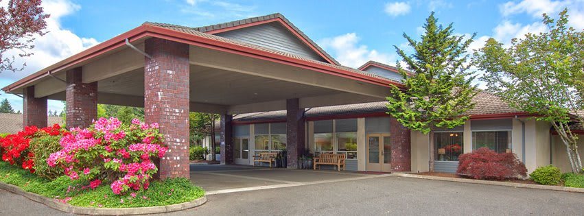 A building entrance with a covered driveway and benches outside.