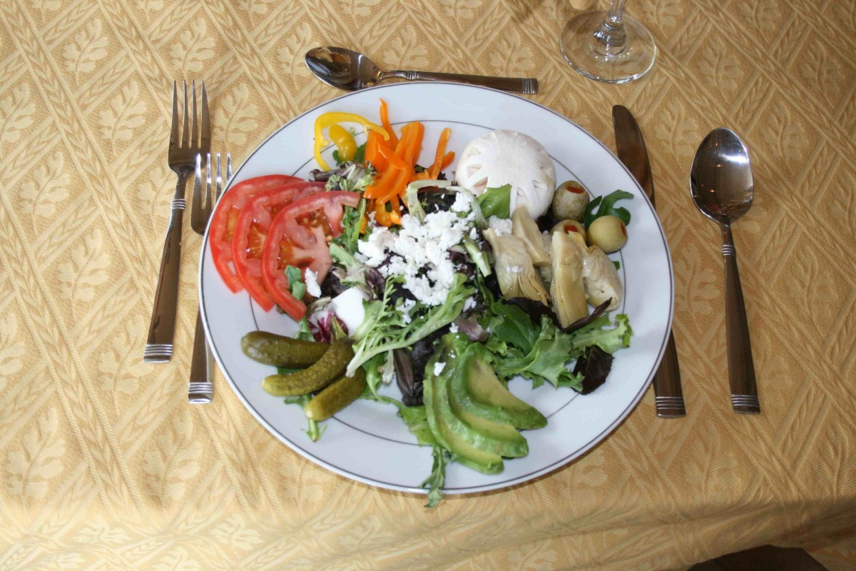 A colorful plate of fresh salad with avocado, tomatoes, carrots, cucumbers, olives, and lettuce.