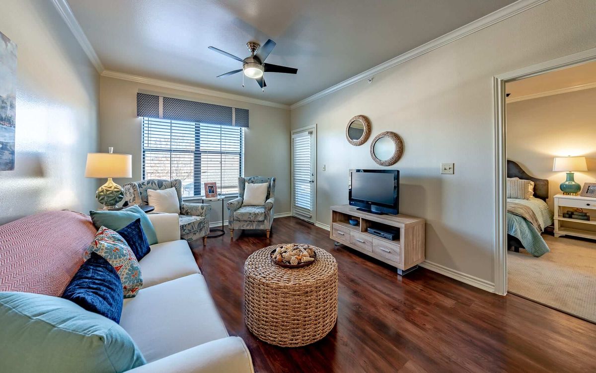 A cozy living room with modern furniture and a television, featuring natural light and warm wooden flooring.