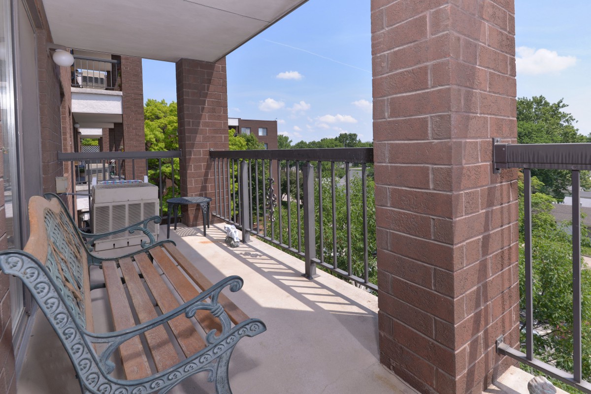 A cozy apartment balcony with outdoor seating and a view of the trees.