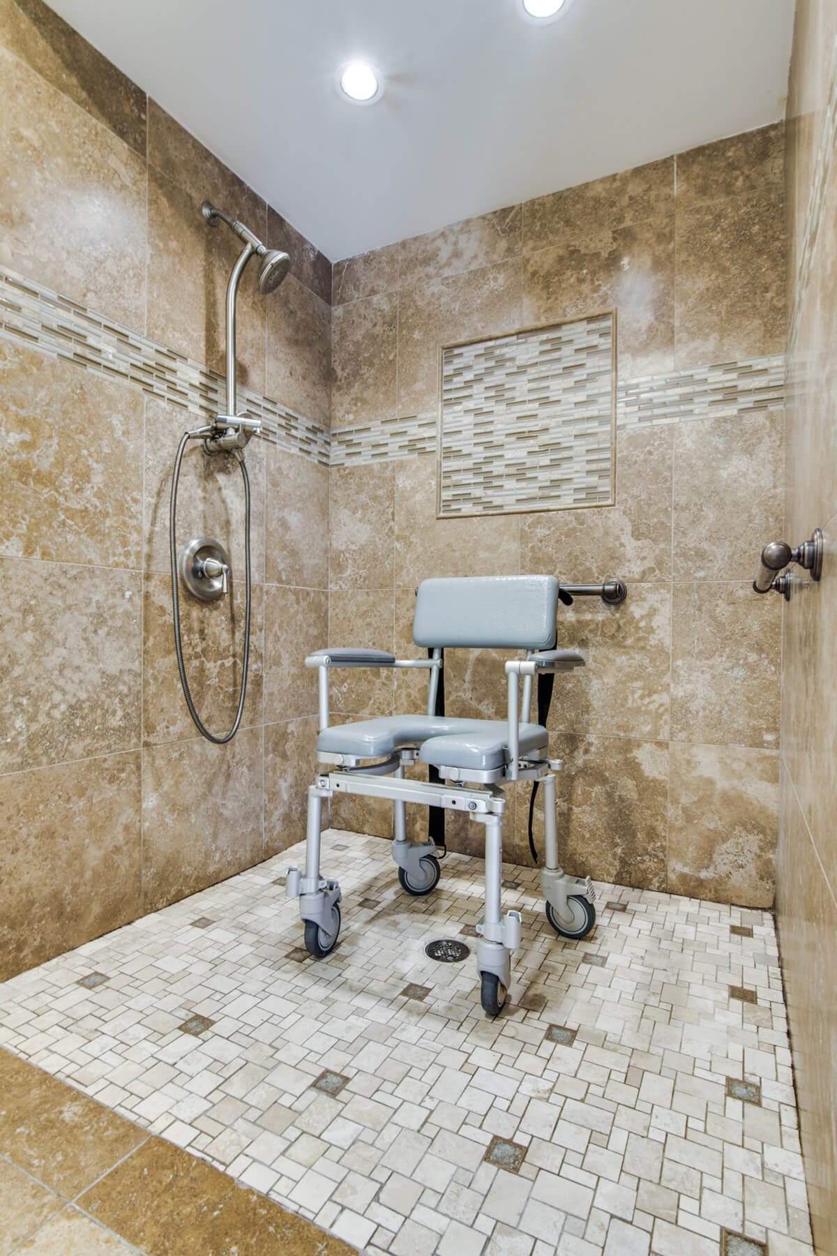 An accessible walk-in shower with a rolling shower chair and decorative tiles.