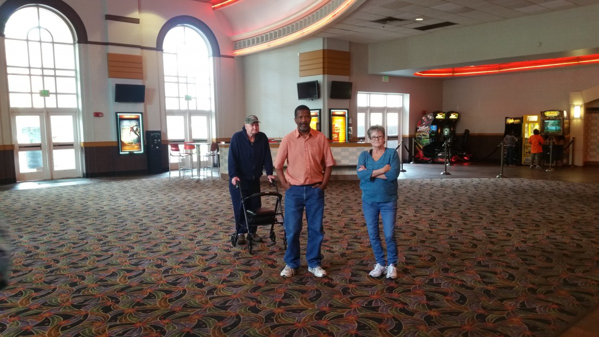 Three people standing in a cinema lobby, with one using a walker.