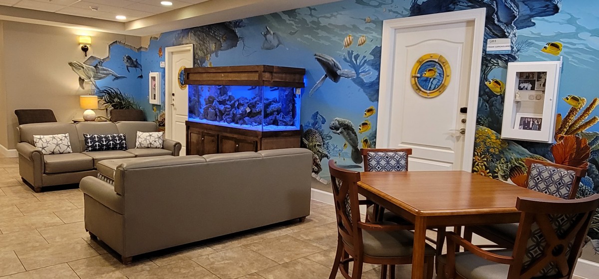 A modern living space featuring a large aquarium and a vibrant ocean-themed mural.