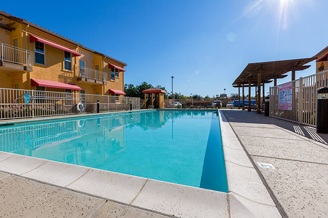 A serene outdoor swimming pool next to a residential or resort building under a clear blue sky.