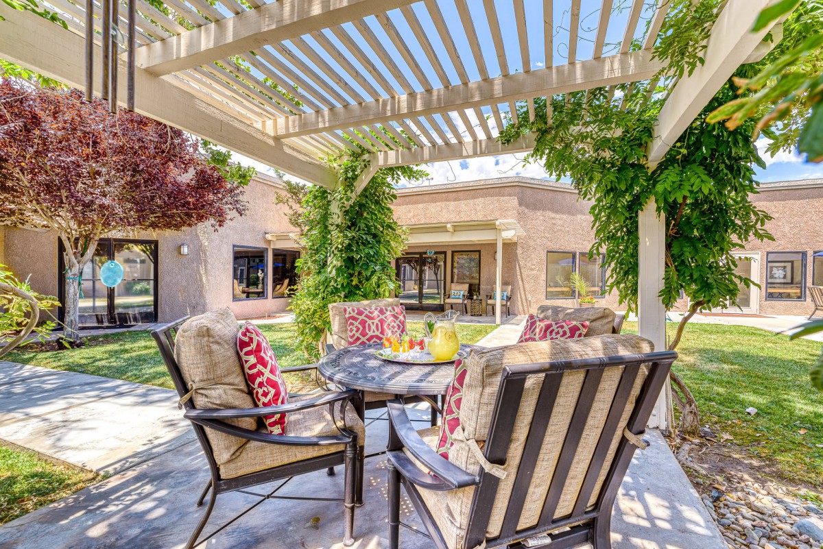 A cozy outdoor patio with a pergola and comfortable seating surrounded by lush greenery.
