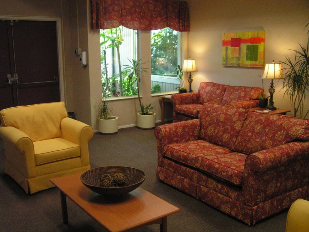 A cozy living room featuring a floral sofa, a yellow armchair, a wooden coffee table with a decorative bowl, and soft lighting from lamps.