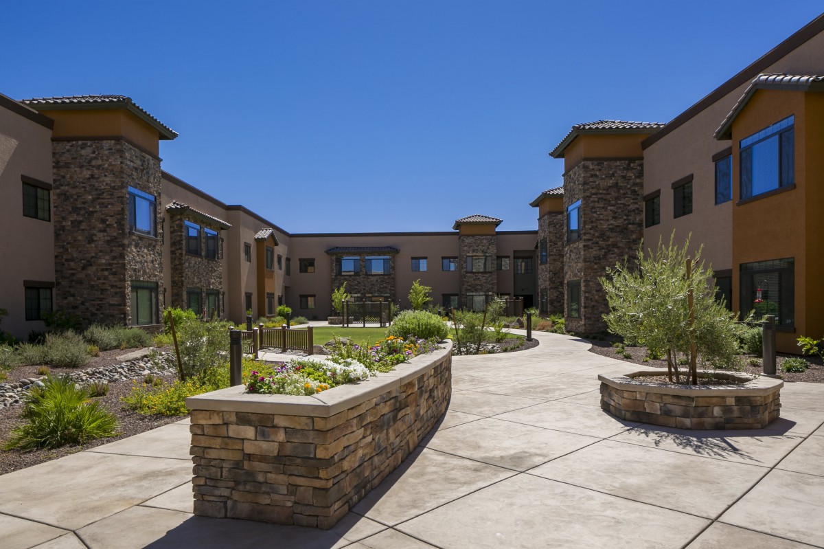 A modern building featuring a landscaped courtyard with stone pathways and greenery under a clear blue sky.