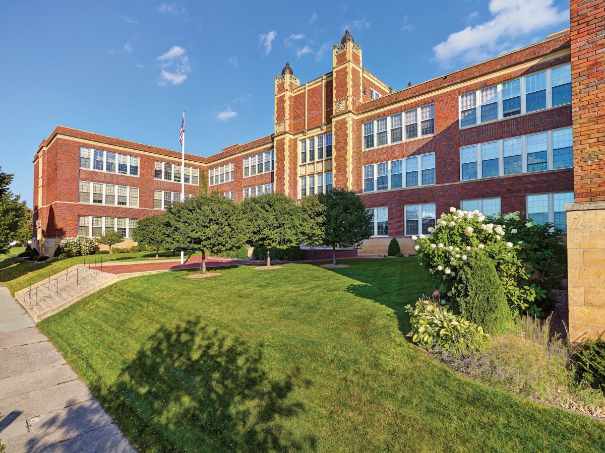 A classic brick school building with a well-maintained lawn and clear blue sky.