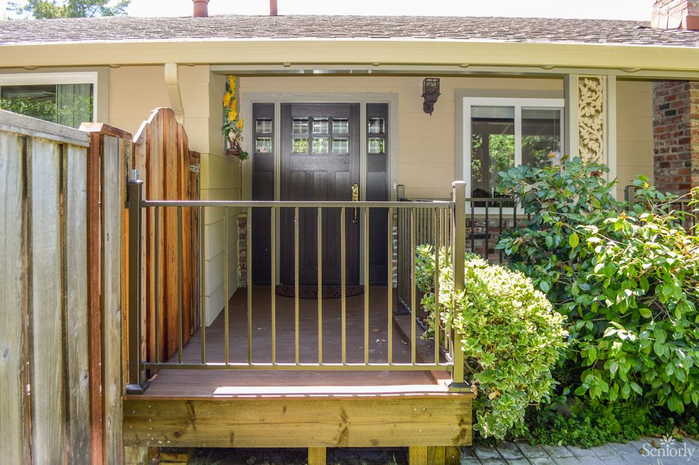 A small porch with railings and a sliding glass door leading to the interior of a house, surrounded by greenery.