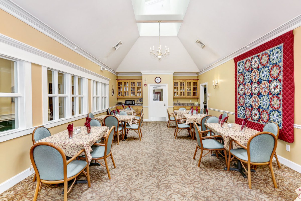 A well-lit dining room with several tables and chairs, featuring large windows and a skylight.