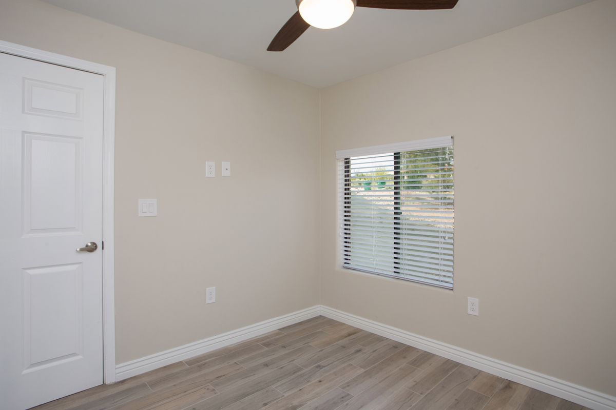 An empty room with hardwood floors, a ceiling fan, and a window with blinds.