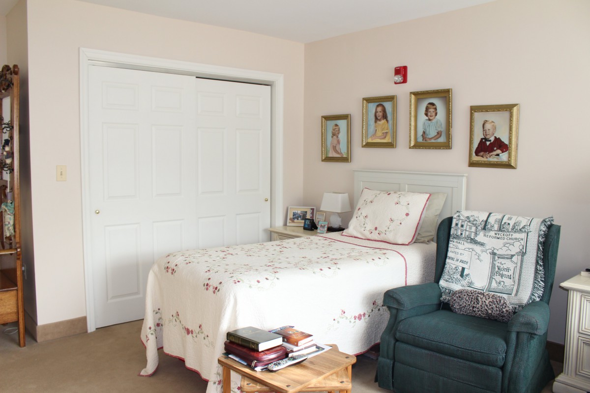 A cozy bedroom with a single bed, a green armchair, and framed pictures on the wall.