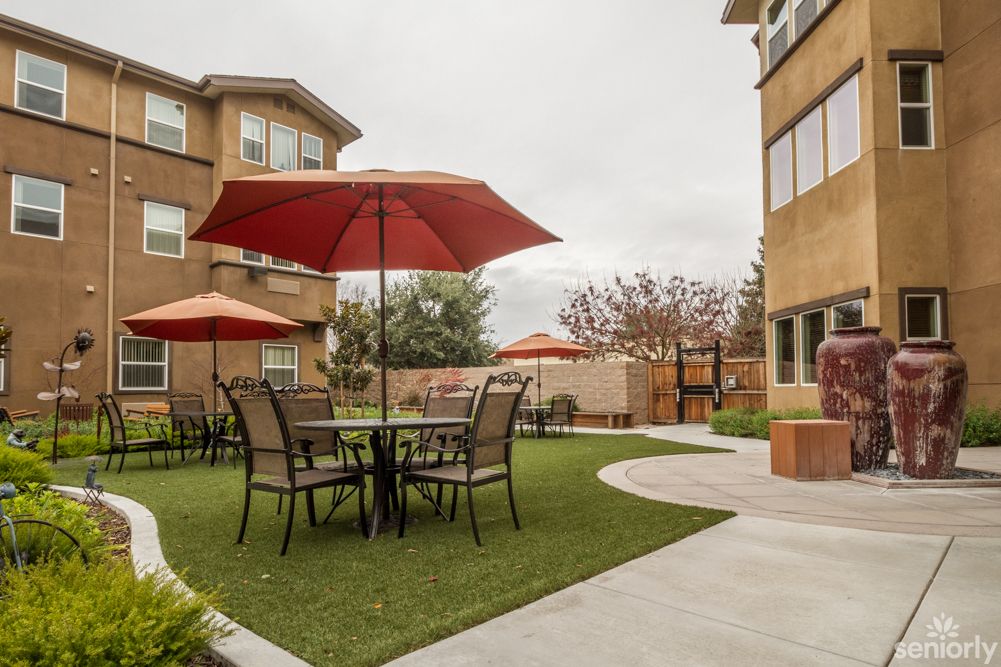A cozy outdoor patio area with tables and chairs under red umbrellas, surrounded by buildings.