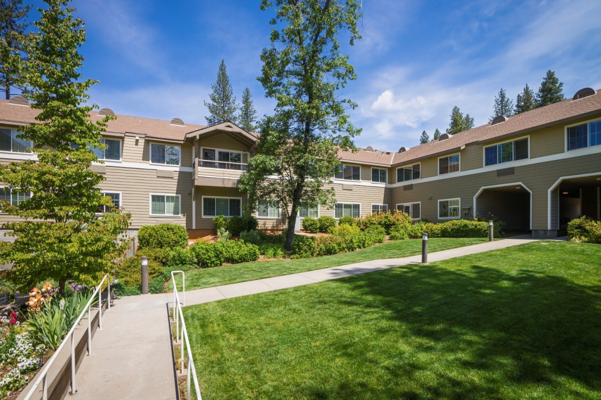 A two-story apartment building with landscaped gardens and a clear blue sky.