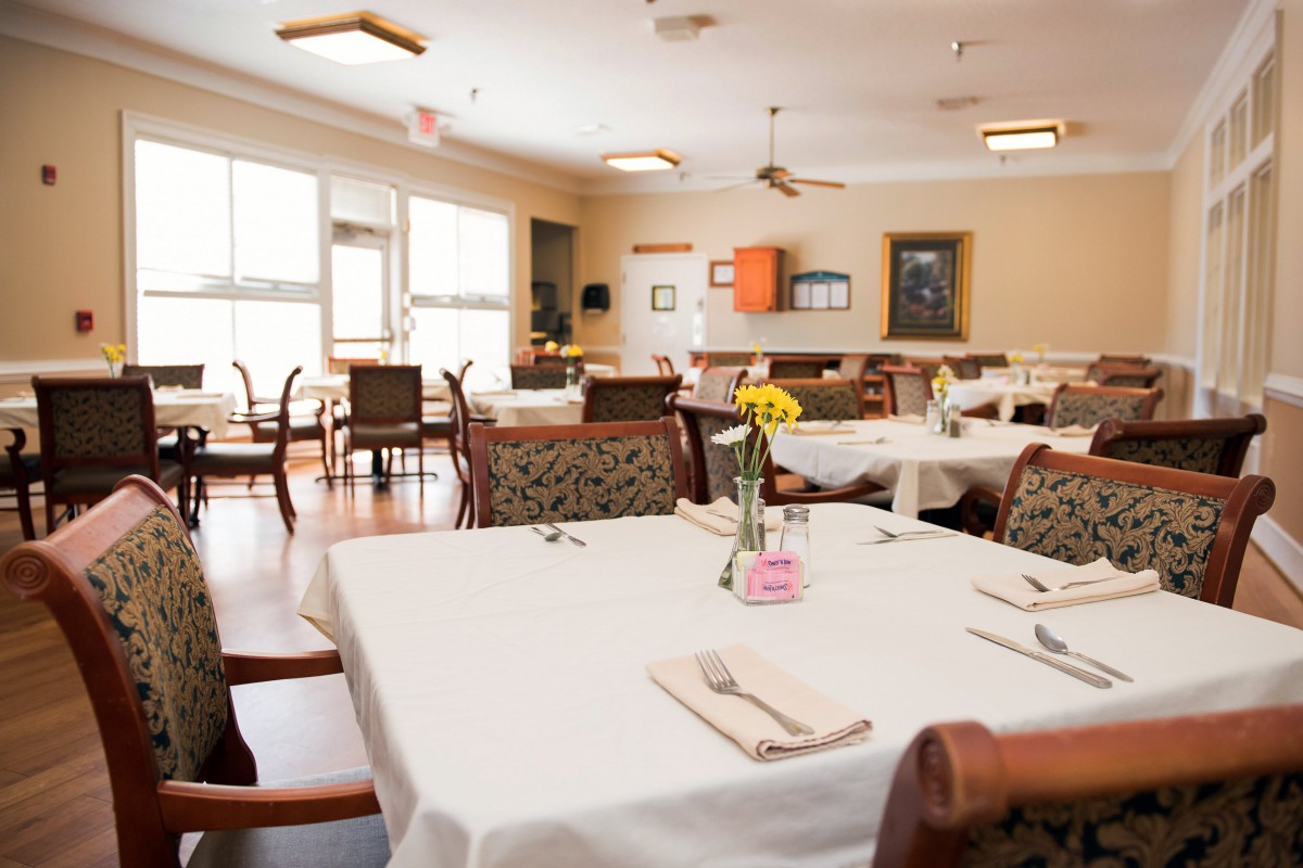 A well-lit dining room with elegantly set tables and chairs, ready for service.