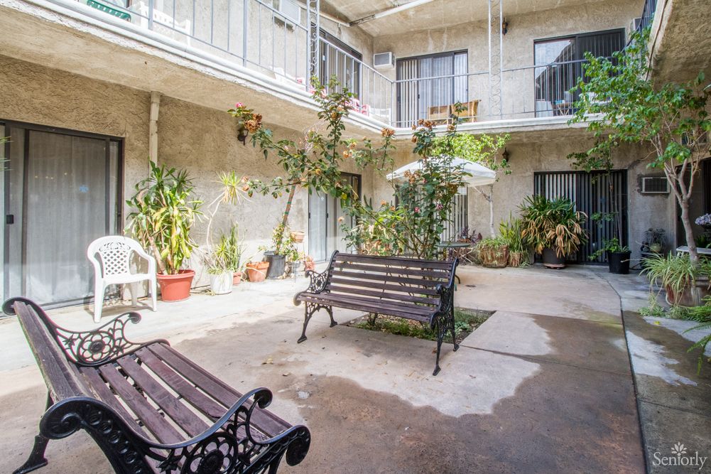 A cozy courtyard with benches, plants, and a patio umbrella, surrounded by apartment balconies.