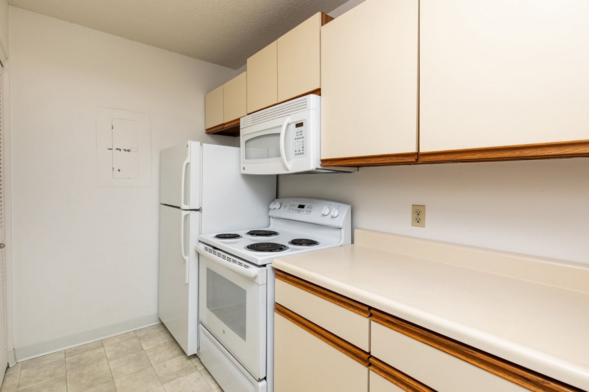A compact kitchen with a refrigerator, stove, microwave, and wooden cabinets.