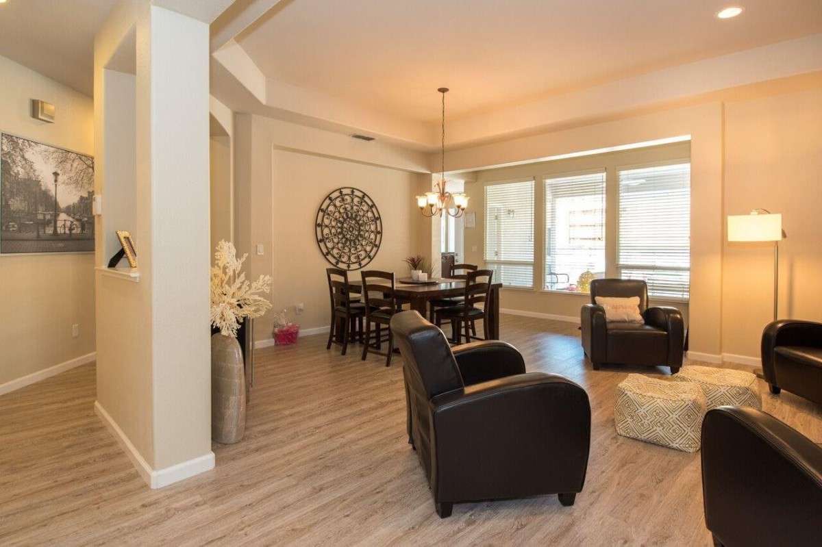 A modern and cozy living room with a dining area, featuring dark furniture and abundant natural light.