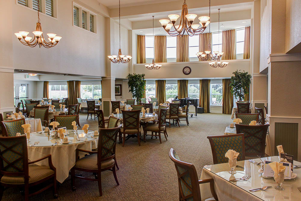 An elegant dining area with multiple round tables, chandeliers, and large windows.