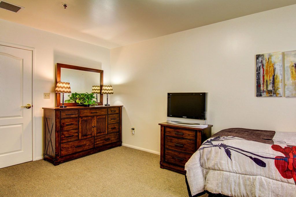 A cozy bedroom featuring a dresser with a mirror, lamps, and a small television on a side table.