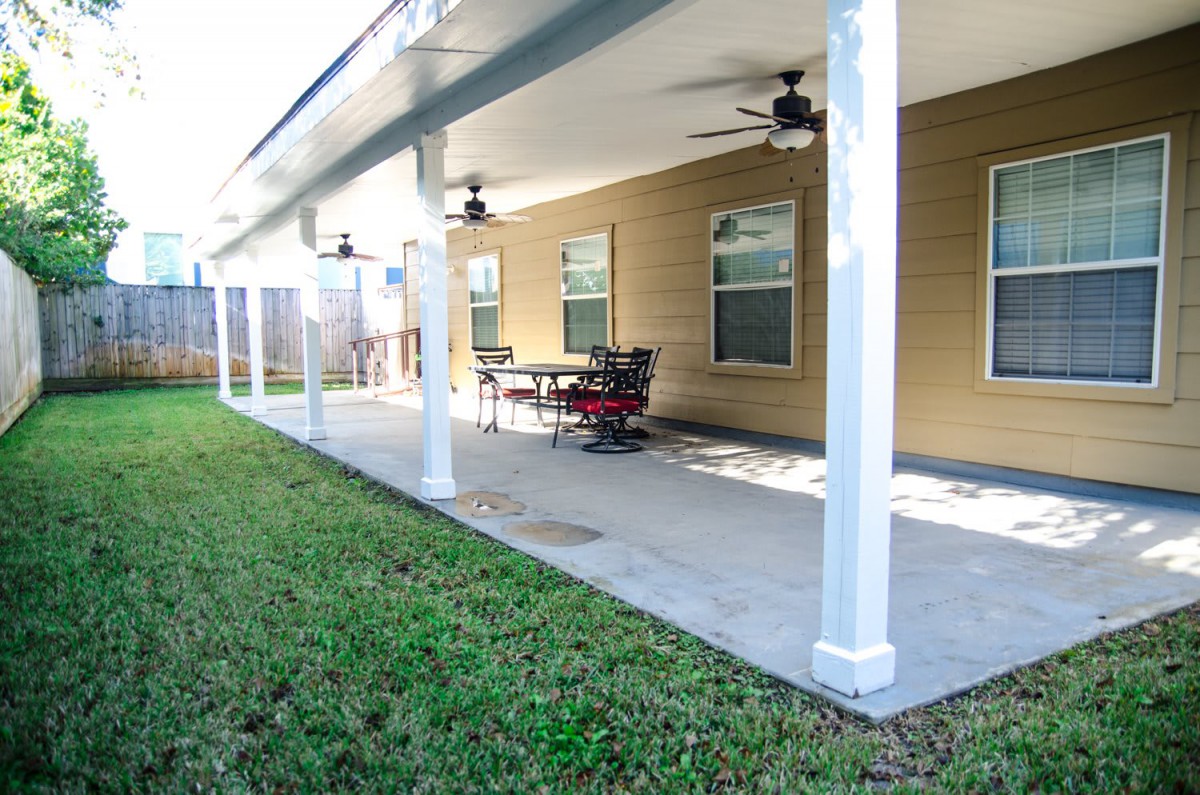 A covered patio with ceiling fans and outdoor furniture adjacent to a grassy lawn.