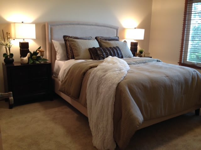 A cozy bedroom with a neatly made bed, flanked by nightstands and illuminated by two lamps.